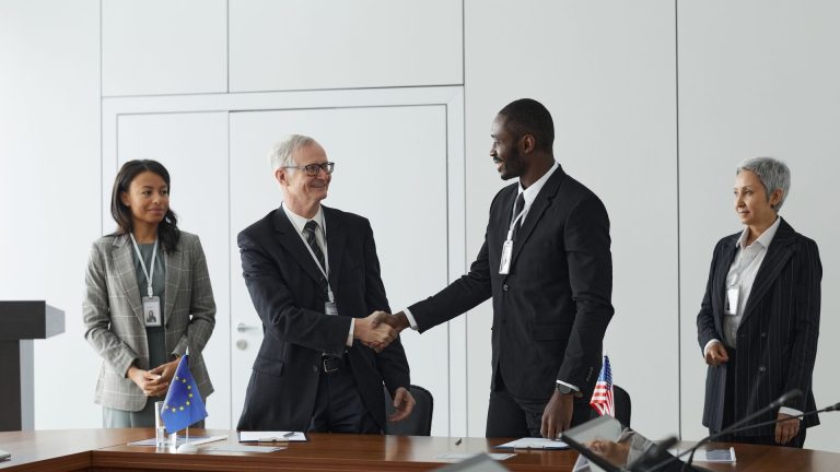 Mediation and Arbitration Strategies for Resolving International Business Disputes Executives shake hands after signing an international agreement, with EU and US flags on the table, illustrating mediation and Arbitration Strategies for Resolving International Business Disputes